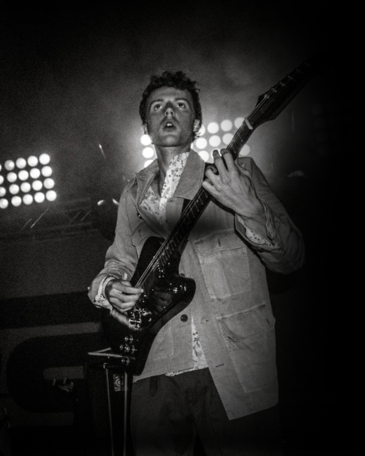 Black and white image of Herbie May playing guitar on stage with lights in the background